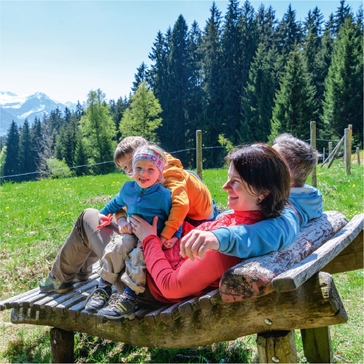 Familie mit zwei kleinen Kindern sitzt auf einer schönen Bank und genießt die Aussicht auf die Alpen
